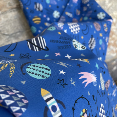 Blast Off Bright Blue Space Cotton Fabric by Dashwood Studios -  a bright blue fabric with space themed design, rockts, shooting stars planets, in pink, turquoise, yellow and black 
